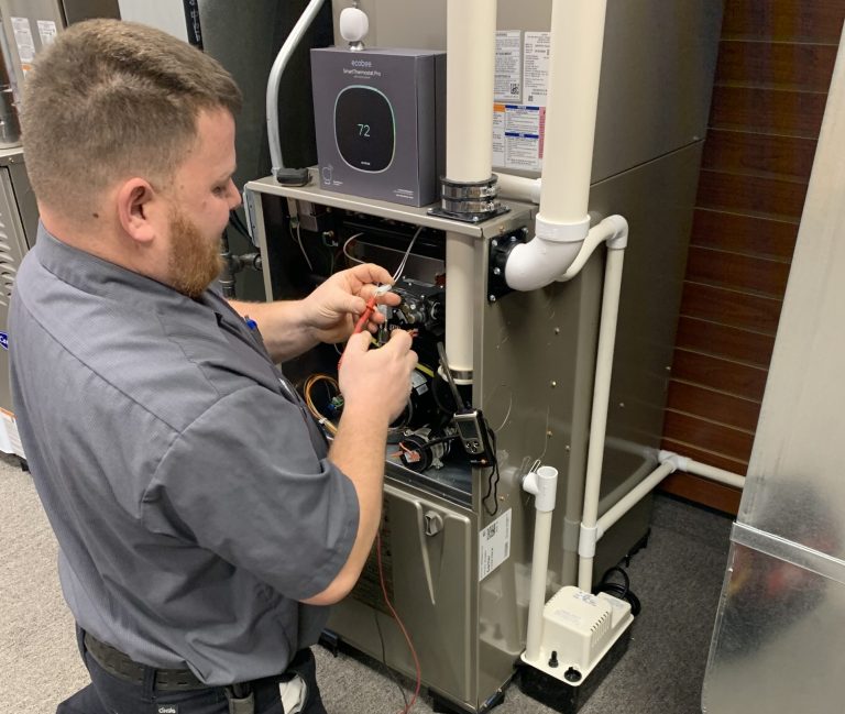 Technician performing maintenance on a gas-fired boiler, inspecting wiring and components for HVAC service.