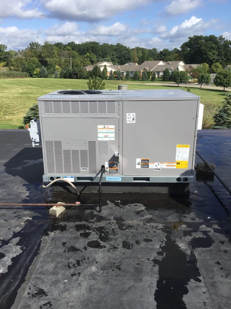 Commercial rooftop HVAC unit on a flat roof, surrounded by green landscape and residential buildings, showcasing quality installation by Mechanical Heating & Cooling.