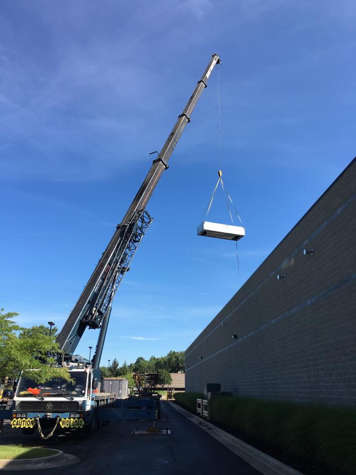Crane lifting rooftop HVAC unit for commercial installation at Mechanical Heating & Cooling site.