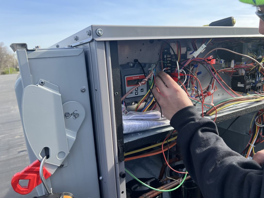 Technician inspecting electrical components inside a commercial HVAC unit, focusing on wiring and connections, ensuring efficient operation and safety.
