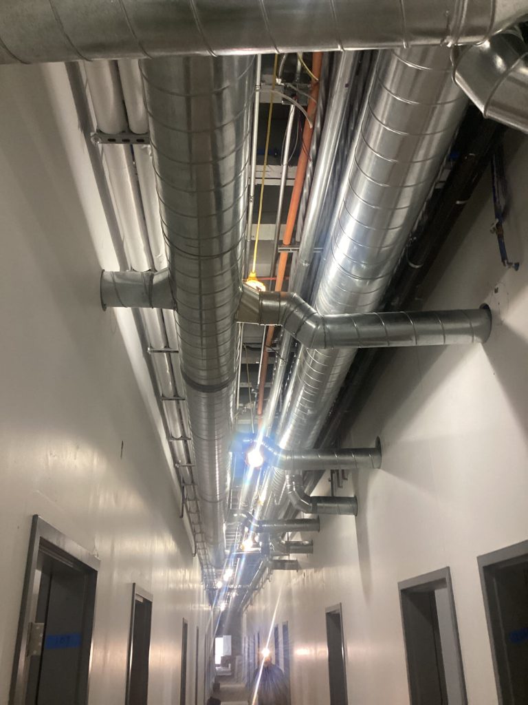 Metal ductwork and piping in a commercial building hallway, illustrating HVAC installation and ventilation systems.