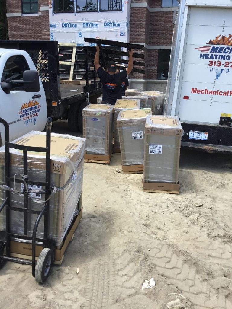Worker unloading HVAC equipment from a truck for installation by Mechanical Heating & Cooling, showcasing new furnace units on-site.