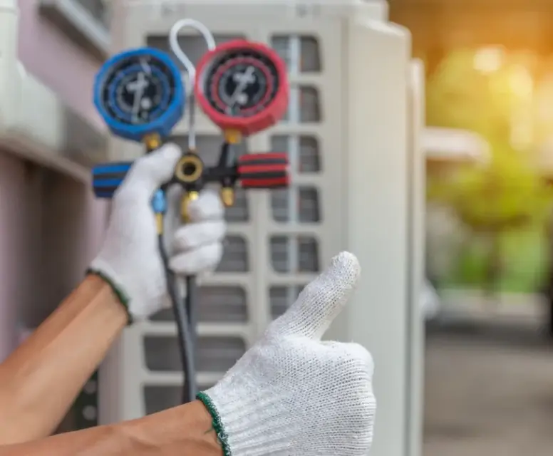 HVAC technician holding pressure gauges and giving a thumbs-up in front of an air conditioning unit, representing professional heating and cooling services in Dearborn Heights.