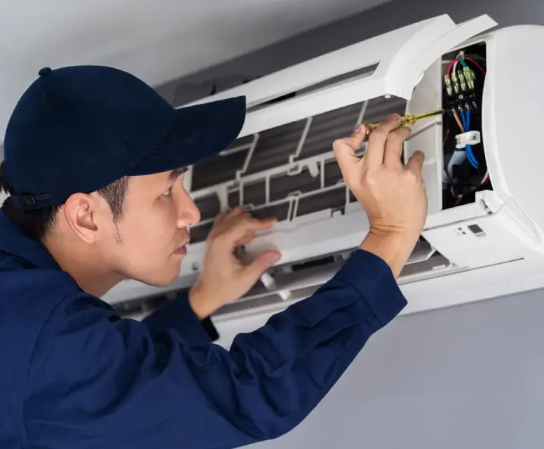 Technician performing AC maintenance on a wall-mounted air conditioning unit, focusing on internal components with a screwdriver, emphasizing HVAC service expertise.