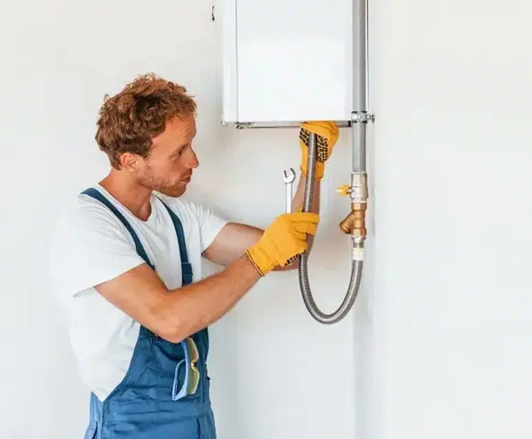 Technician installing a tankless water heater, wearing gloves and using a wrench, in a home setting.
