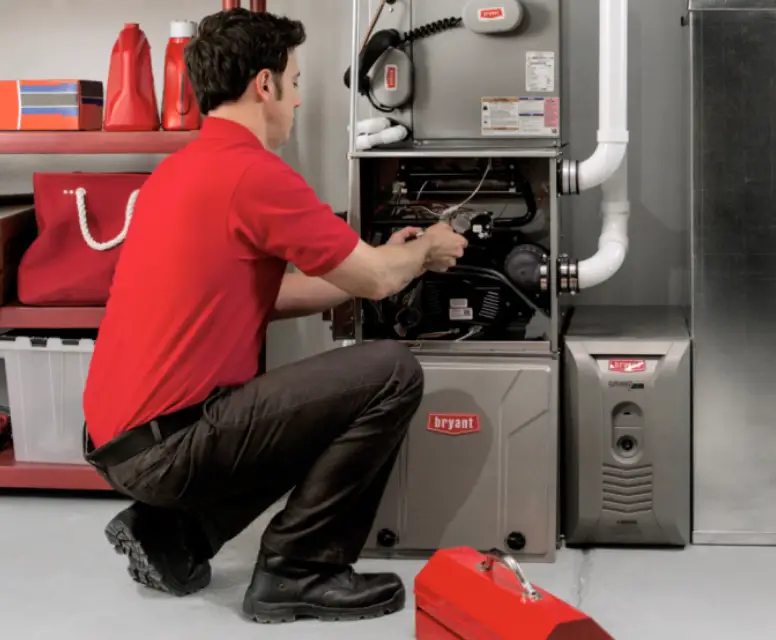 HVAC technician in a red shirt servicing a Bryant furnace, demonstrating maintenance and repair expertise for heating systems.