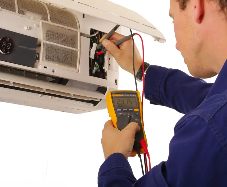Technician performing maintenance on a wall-mounted air conditioning unit, using a multimeter to check electrical connections and ensure optimal performance.